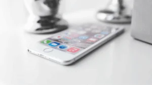 Smartphone on a desk with screen showing colorful app icons, blurred espresso maker in background.