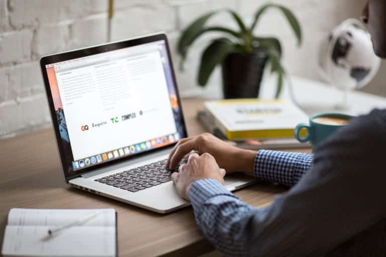 Person working on a laptop with documents and a coffee cup on the desk.