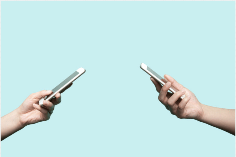 Two hands holding smartphones against a light blue background.