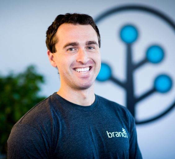 Branch CEO Alex Austin smiling at camera in a Branch t-shirt in front of the Branch logo glyph