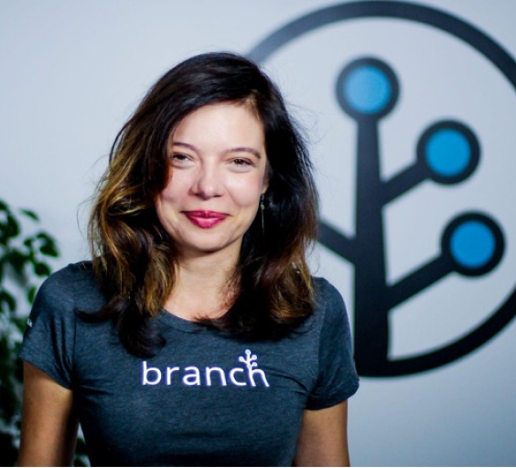 Branch Co-founder Mada Seghete smiling at camera in a Branch t-shirt in front of the Branch logo glyph