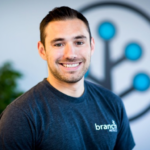 Branch Co-founder Mike Molinet smiling at camera in a Branch t-shirt in front of the Branch logo glyph