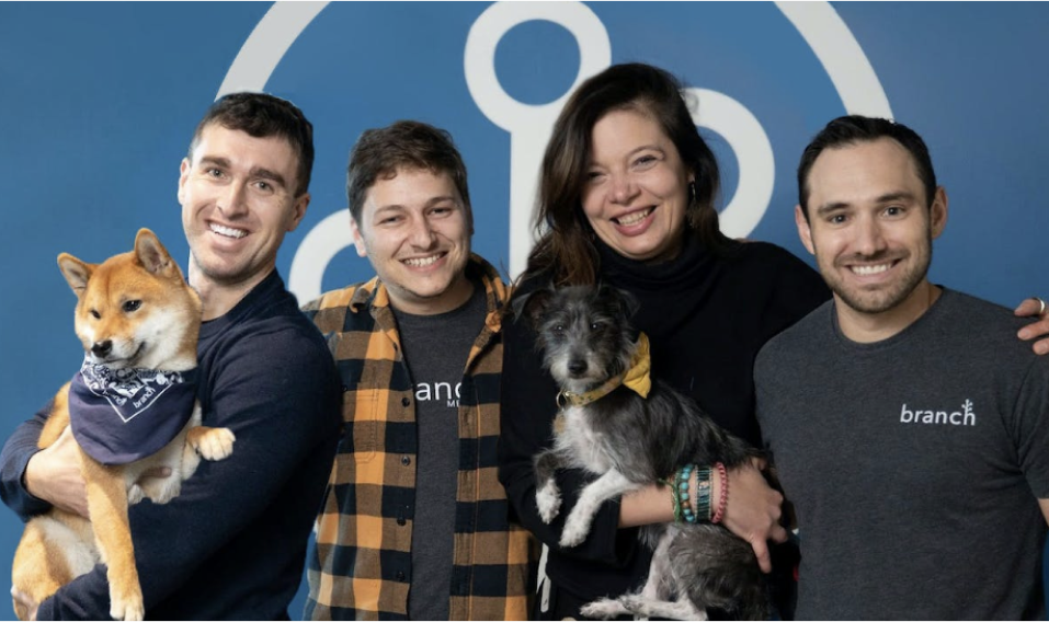 Branch's four founders plus Alex's dog Maple smiling at the camera in front of the Branch glyph logo