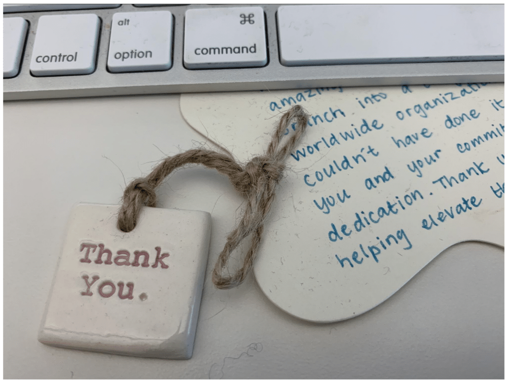 Ceramic tag with "Thank You." on a desk beside a handwritten note and keyboard.