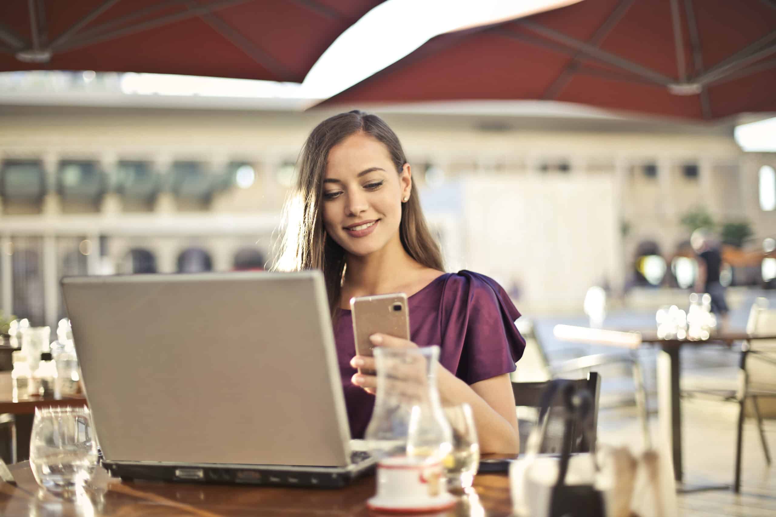 Woman at an outdoor cafe using a laptop and smartphone.