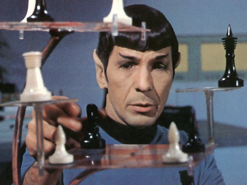 A person reaches out to a futuristic chess set with transparent layers, featuring black and white chess pieces in a sci-fi setting.