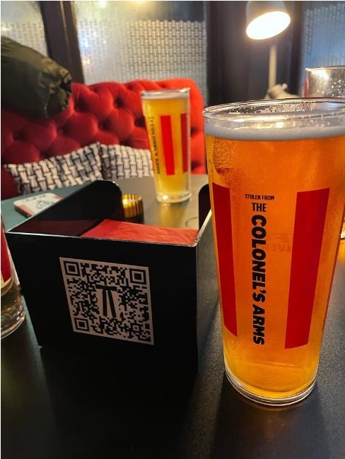 Photograph of a beer next to a napkin holder that has a KFC app QR code displayed on it.